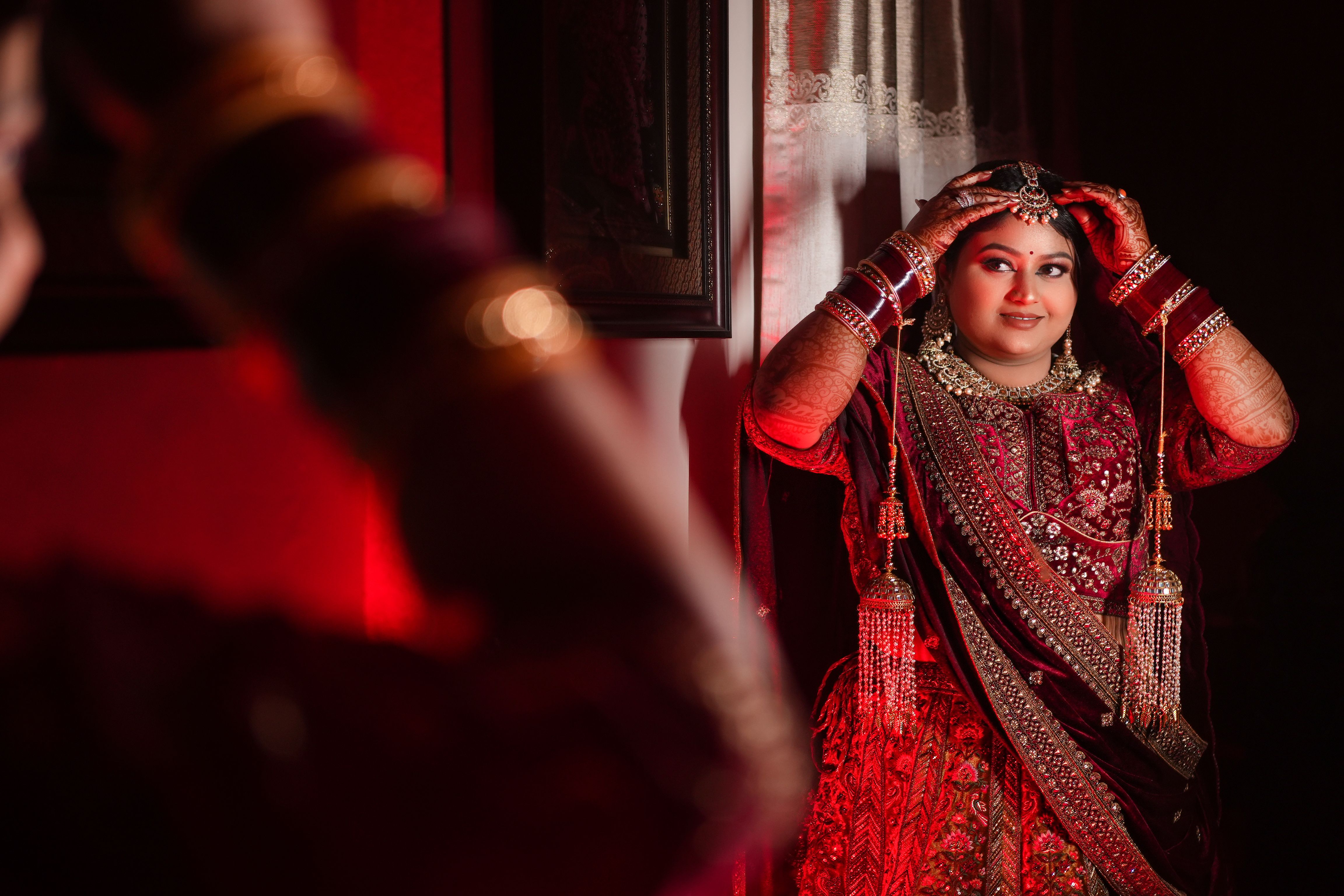 Beautiful Indian bride in traditional red gown adjusting jewelry in Varanasi, India.