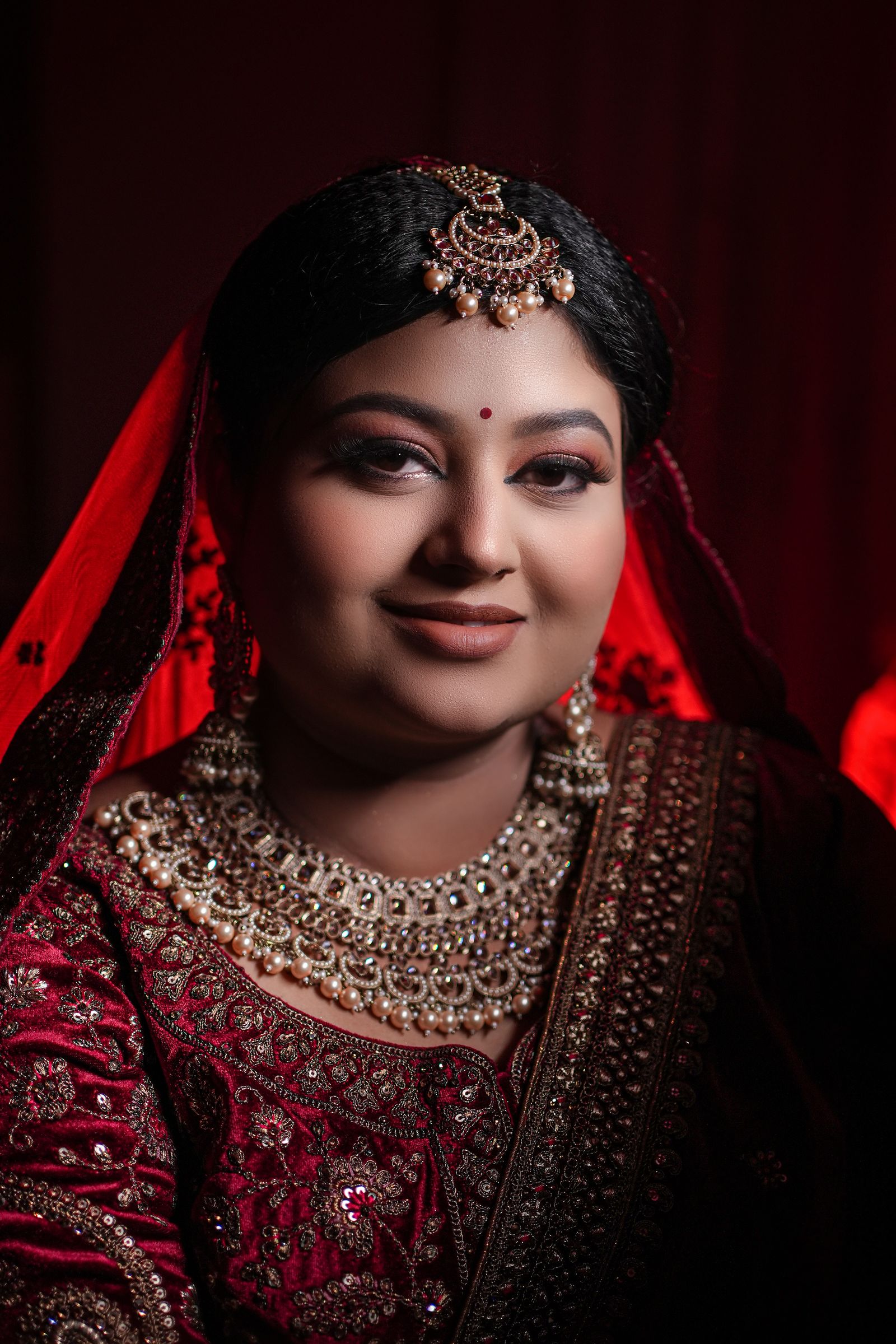 A bride in deep maroon velvet and kundan jewellery, lit low and close.