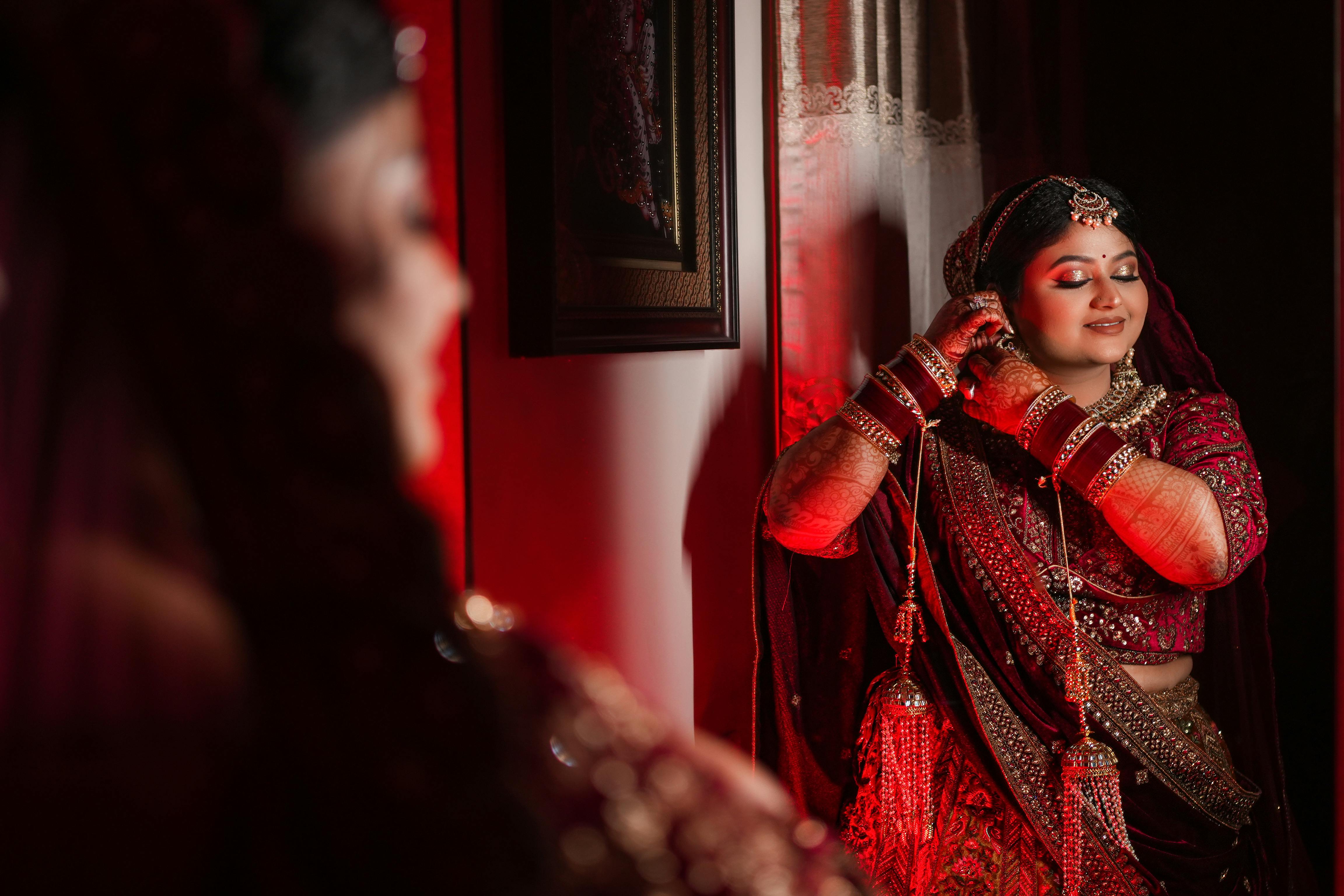 Indian bride in a red gown with traditional jewelry, captured in an elegant bridal pose.