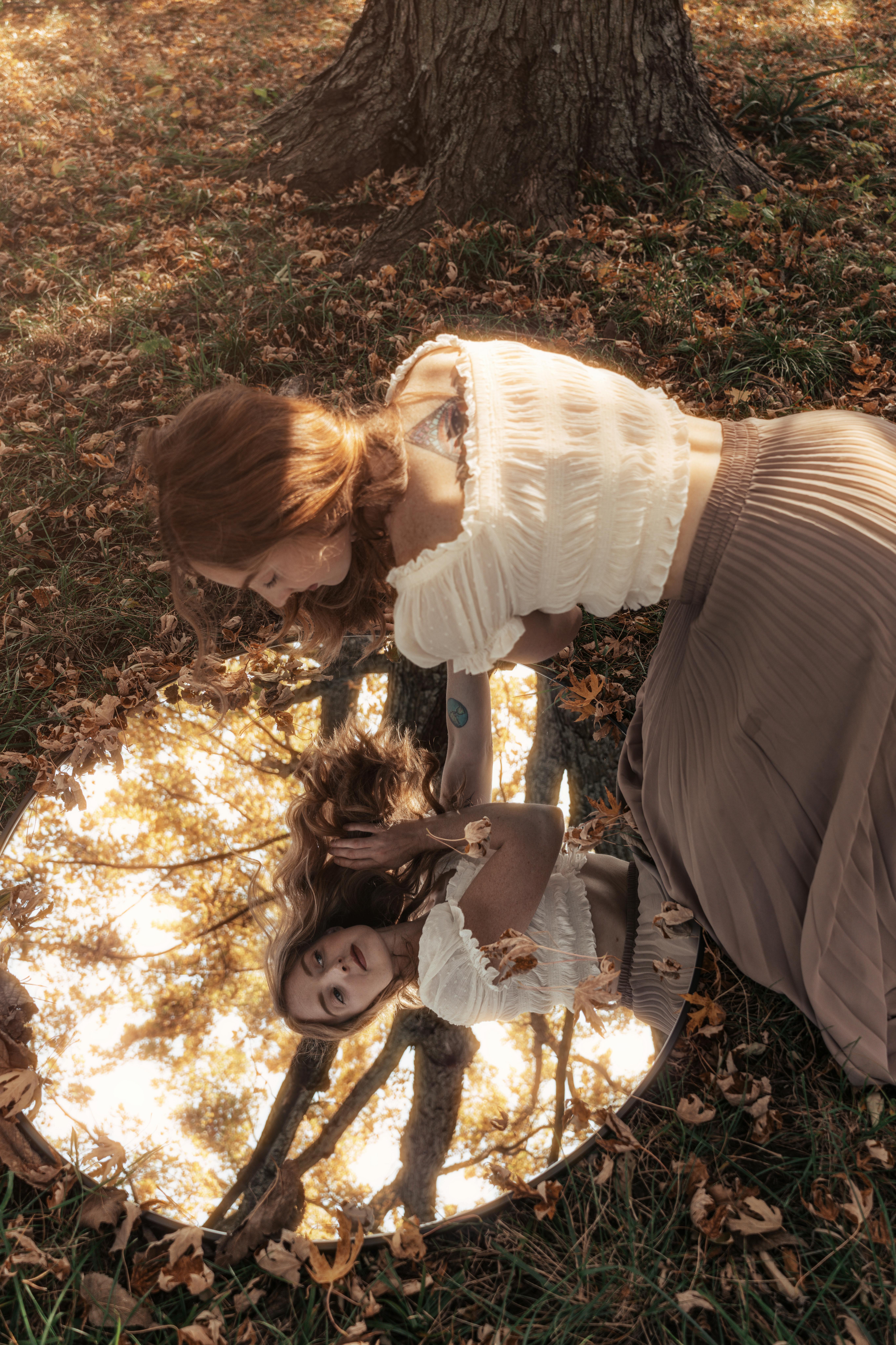 A woman gazes into a mirror surrounded by fall leaves, capturing a serene moment.