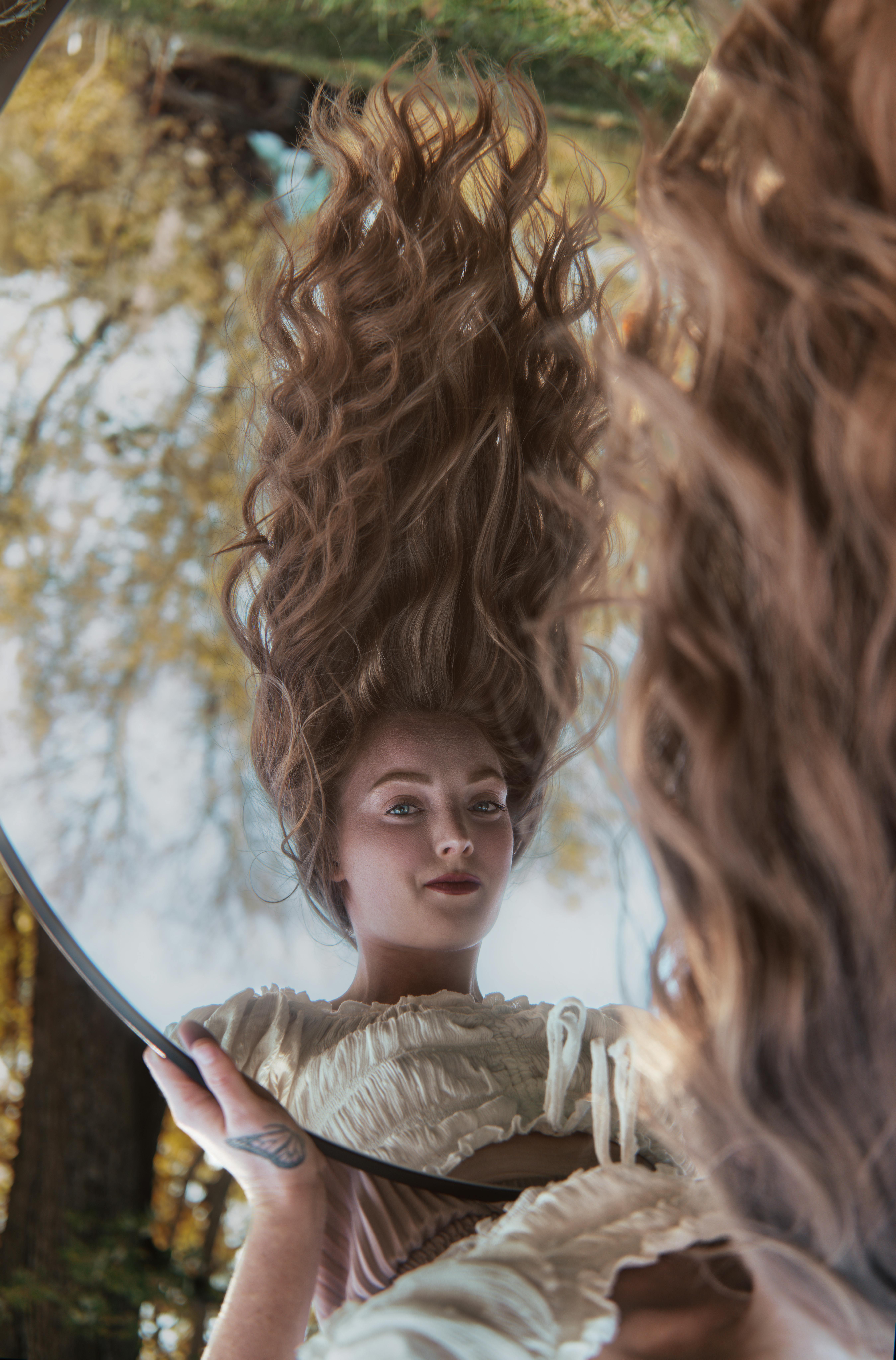 Portrait of a woman with long hair reflected in a mirror outdoors, surrounded by nature.