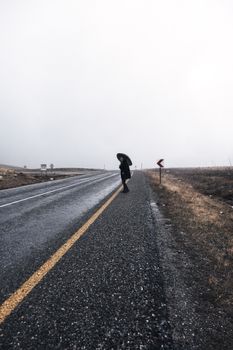 A solitary person with an umbrella walking on a desolate road during a cloudy day.