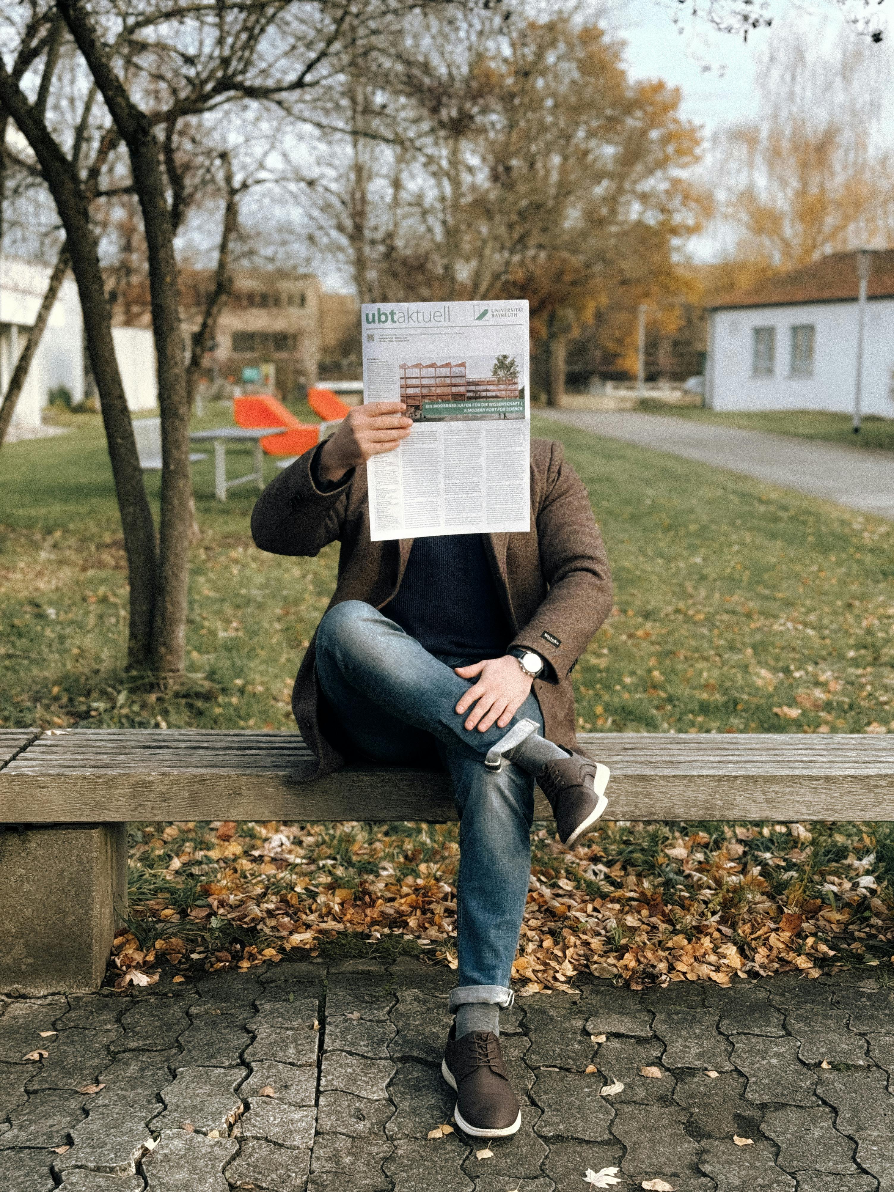 person reading newspaper on park bench in fall