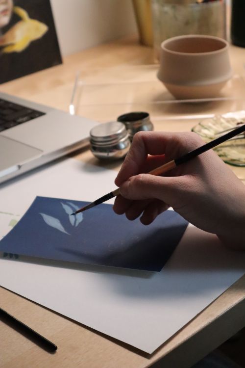 Free Hand painting with brush on blue canvas in artistic workspace. Stock Photo