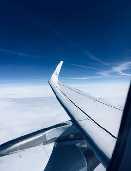 View from an airplane window capturing a sleek wing flying above the clouds on a clear day.