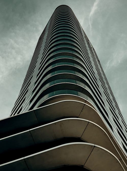 Free Dramatic view of a modern skyscraper with curved architecture against a cloudy sky. Stock Photo