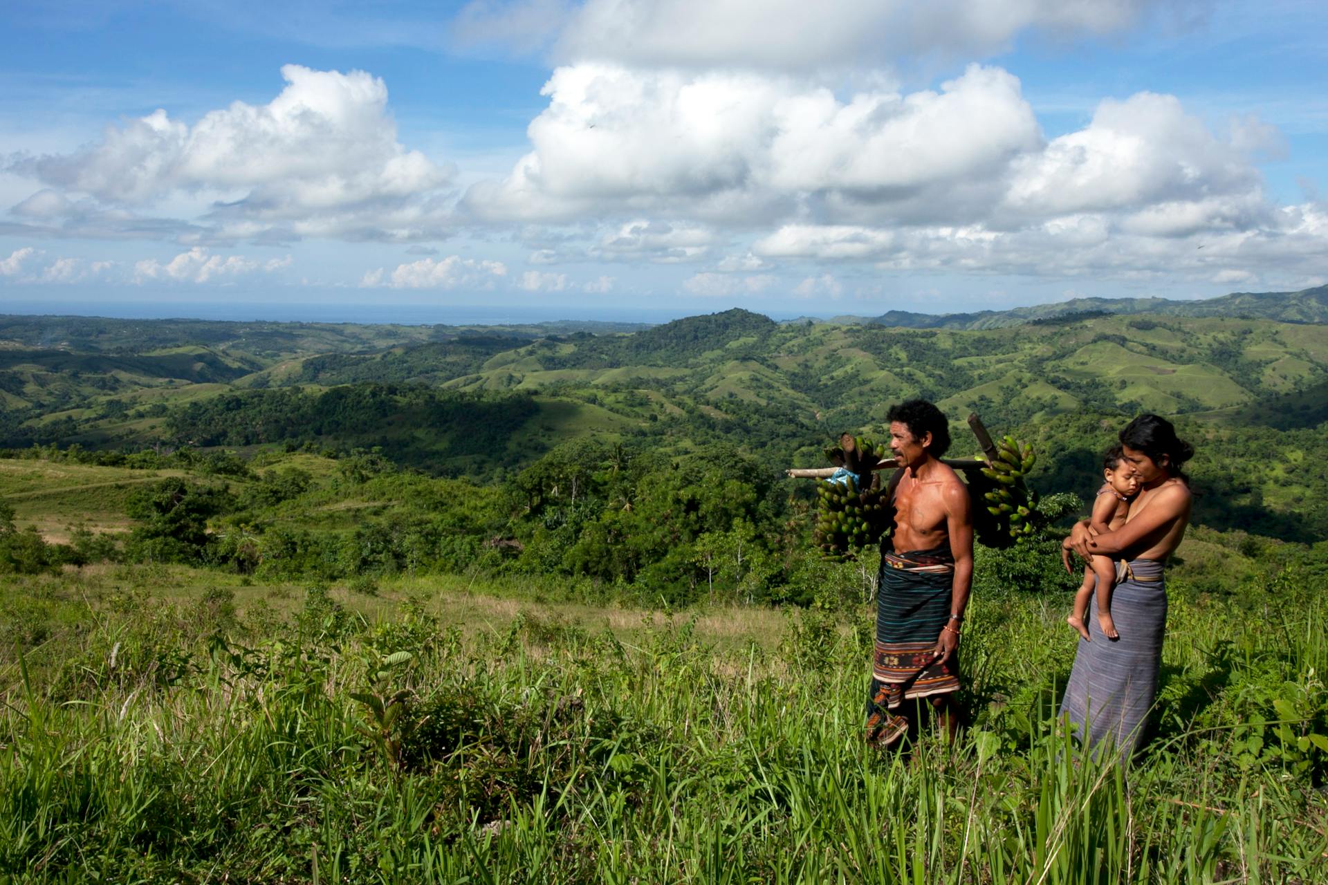 A family of three enjoys a scenic view in the lush countryside, surrounded by hills and open skies.