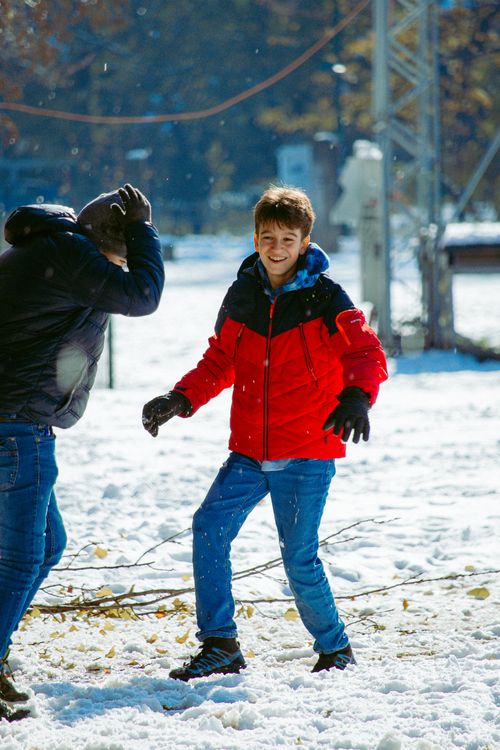 Free Two children laughing and playing a snowball fight in a sunlit snowy park. Stock Photo