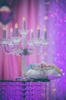 An elegant crystal candelabra alongside a decorative tiara, set against a purple backdrop.