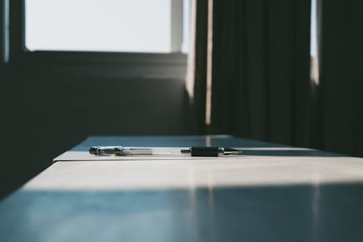 A ballpoint pen resting on a sunlit desk, casting shadows in an empty classroom.