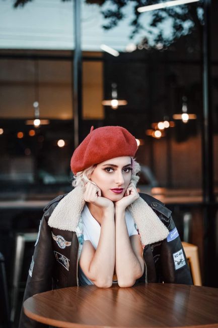 Fashionable woman in red beret posing at a cafe table, exuding urban charm.