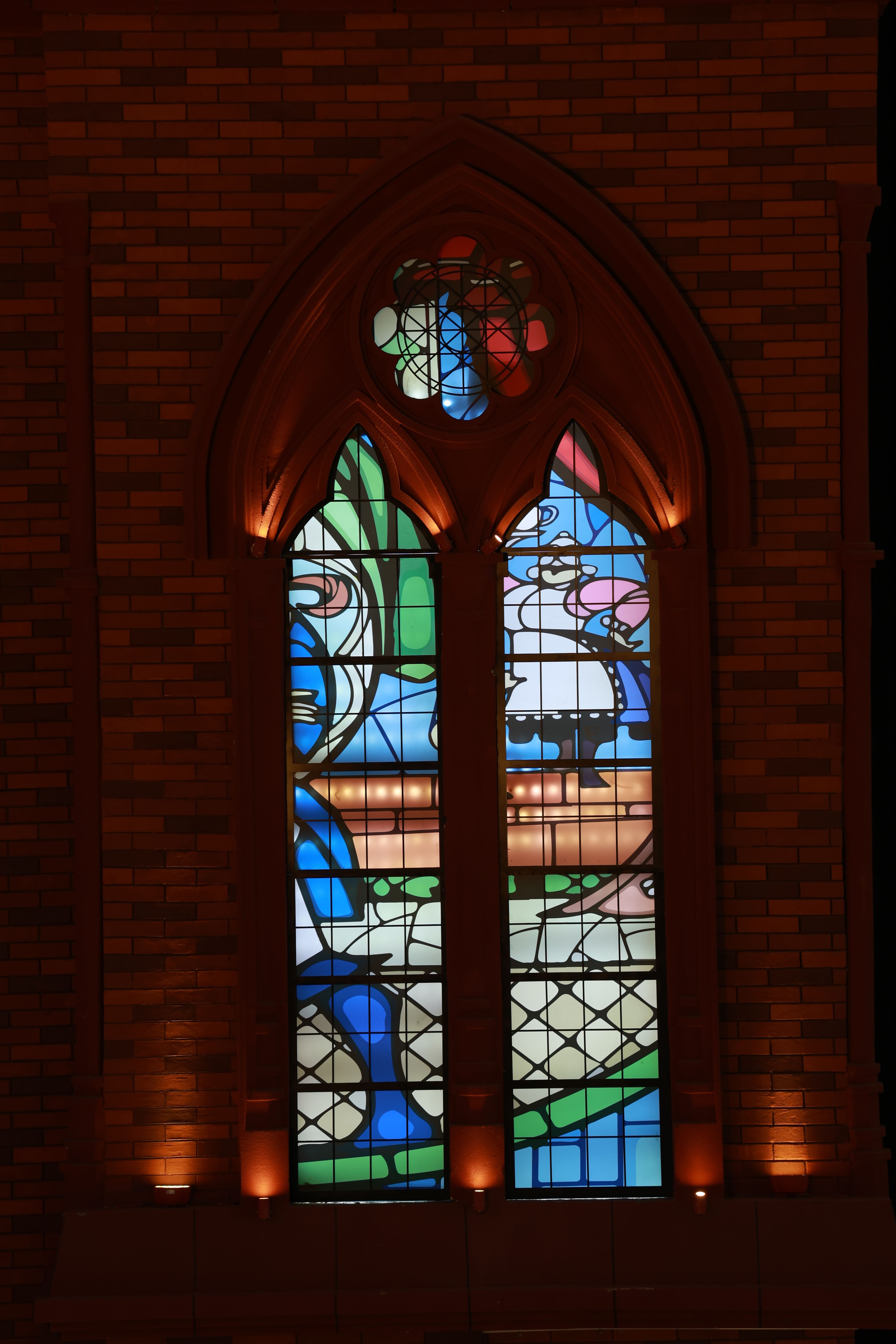 Beautifully lit stained glass window with colorful geometric patterns in a cathedral setting.