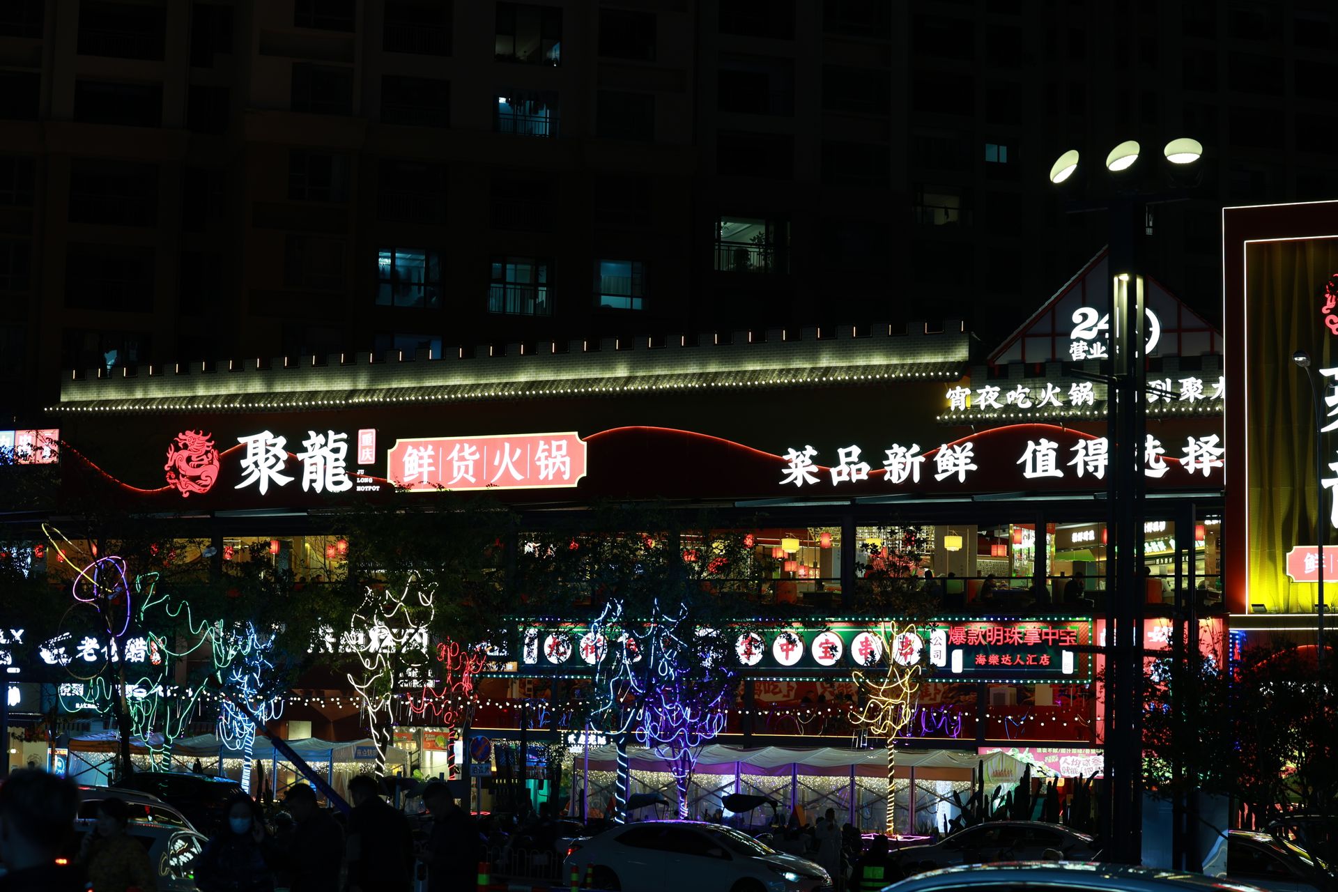 Illuminated Asian street market at night with colorful lights and signage.