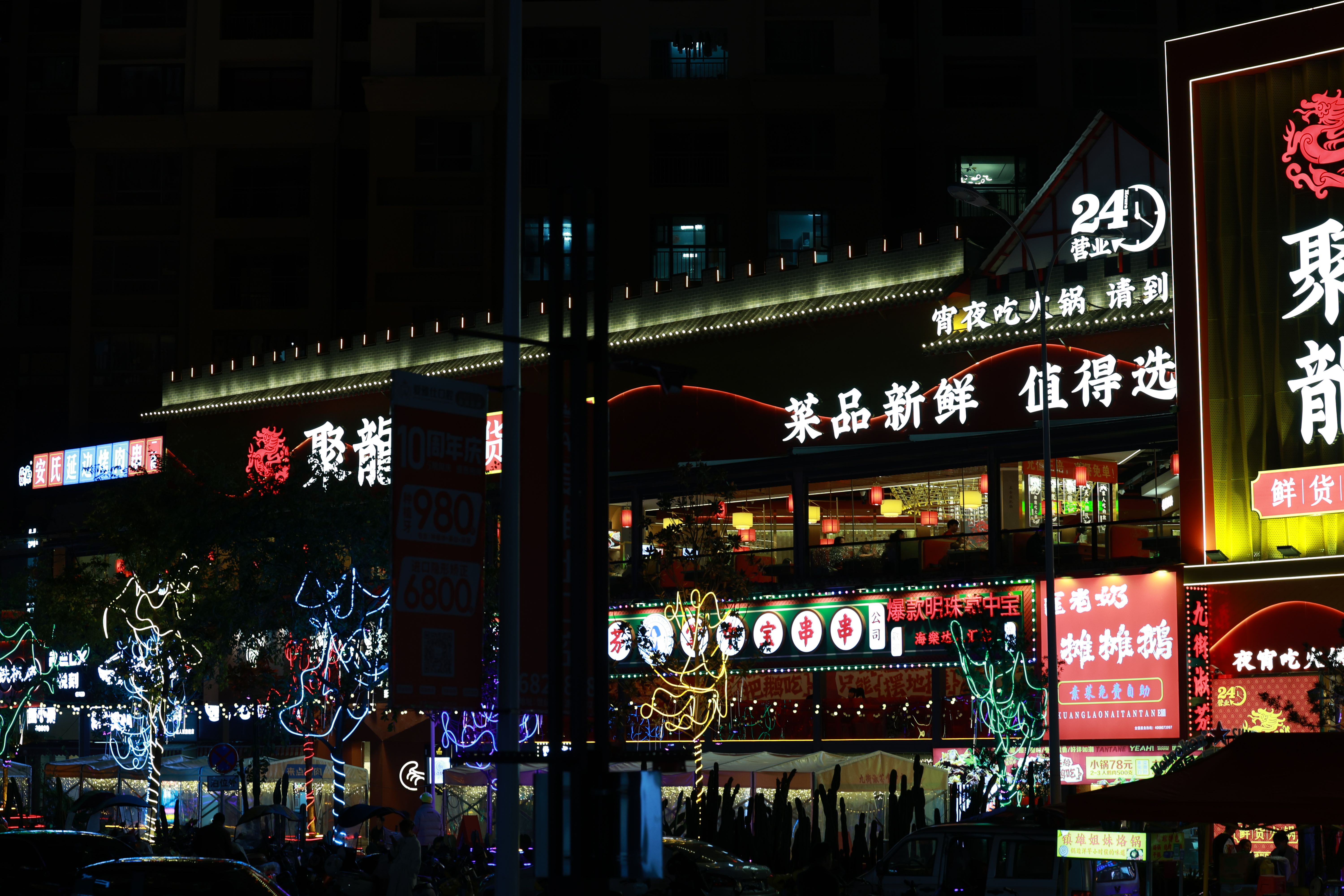 Colorful neon-lit street market bustling with nightlife and Chinese signage.