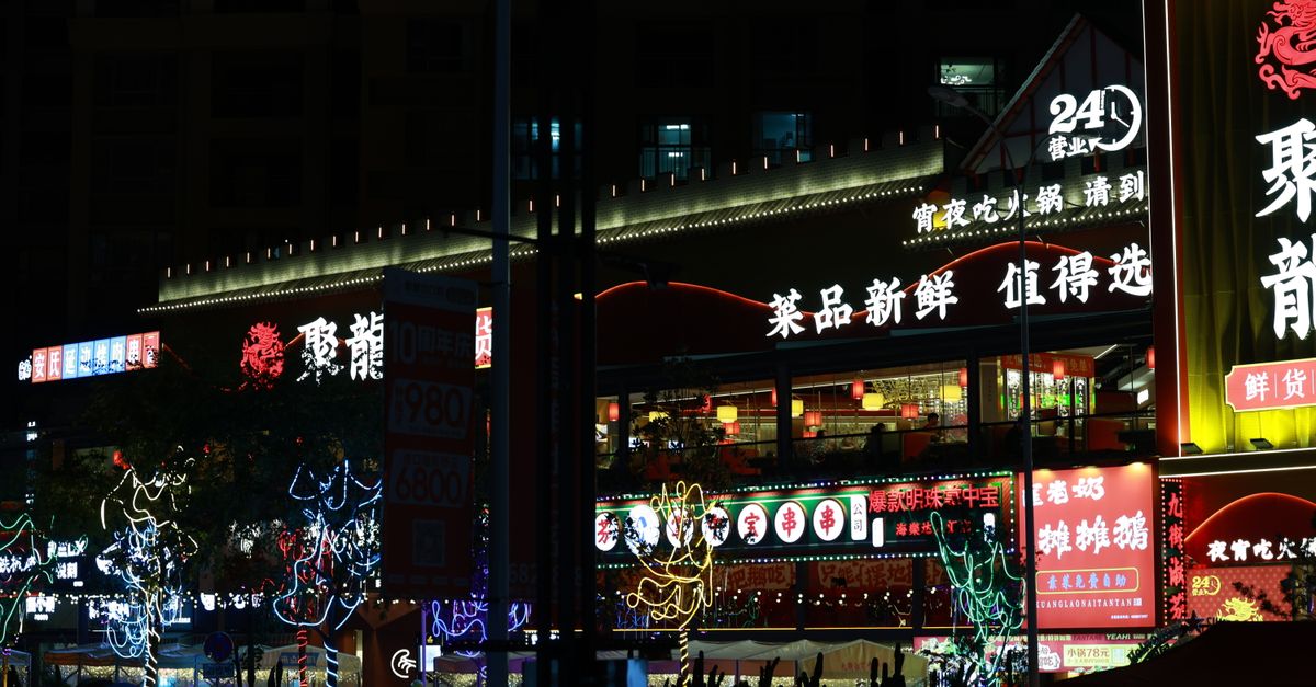 Colorful neon-lit street market bustling with nightlife and Chinese signage.