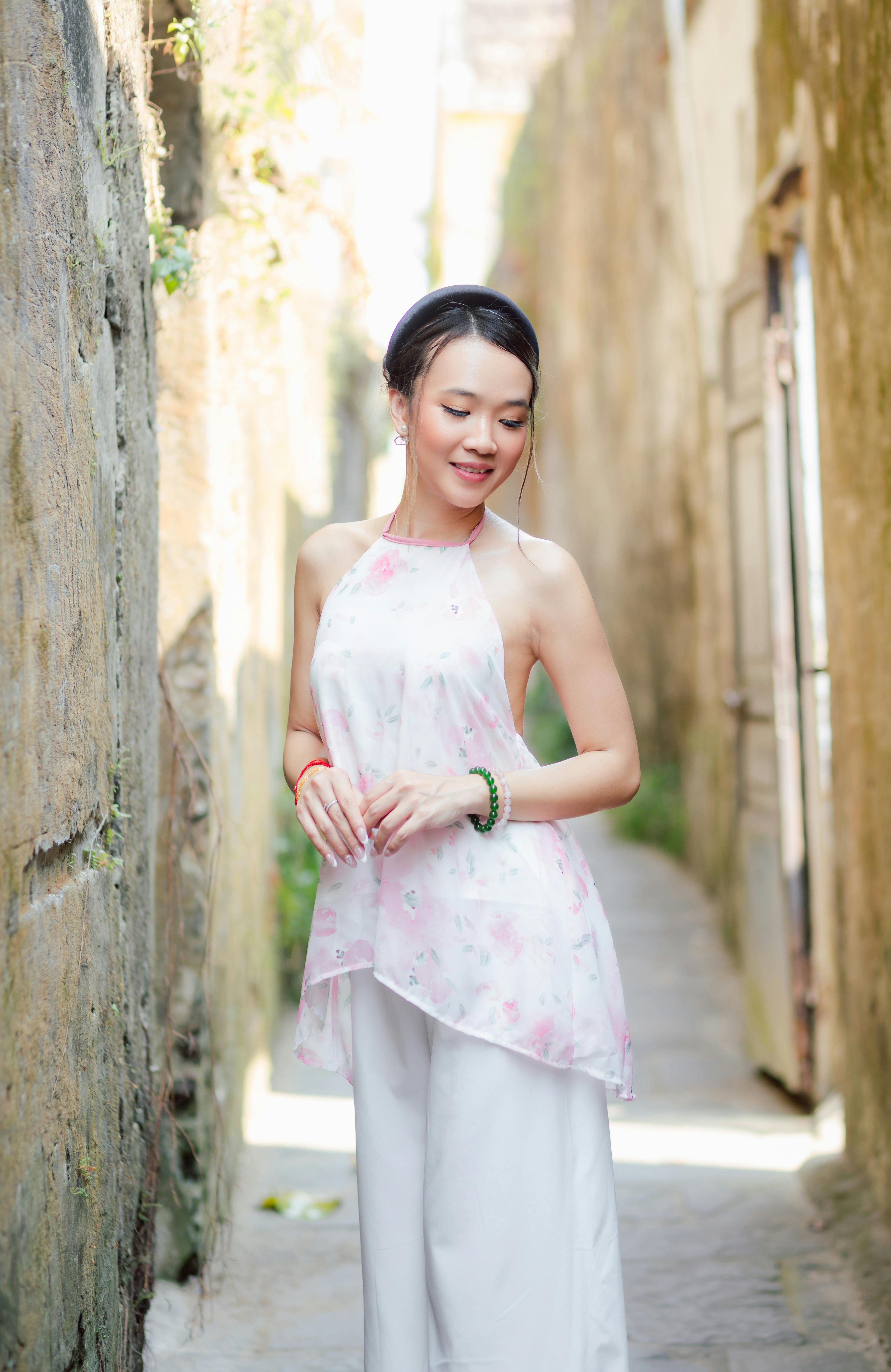 Gratis En kvinne i en hvit blomsterkjole poserer i en pittoresk bakgate i Hội An, Vietnam. Arkivbilde