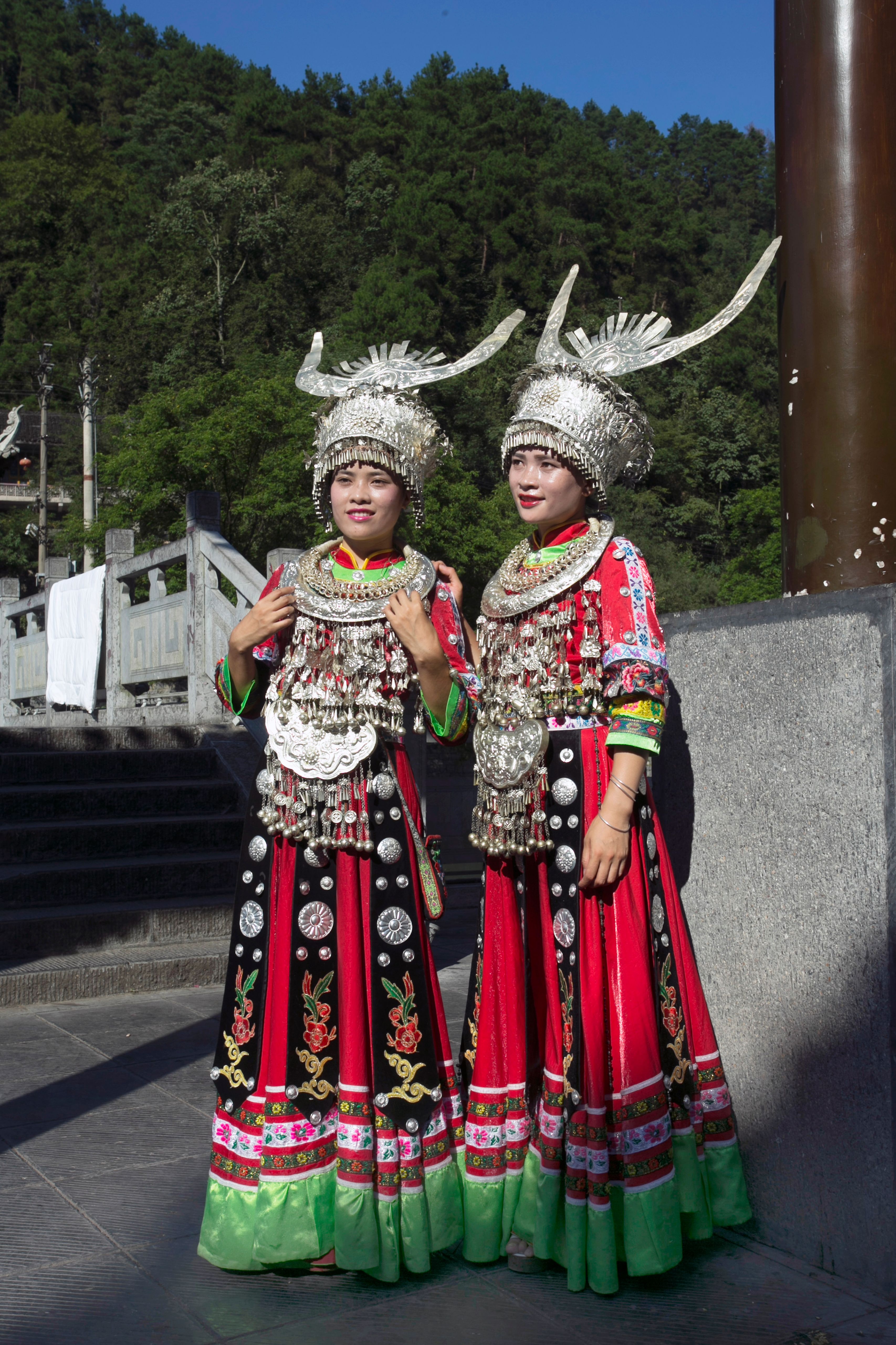 Two Miao women in traditional attire posing outdoors, showcasing cultural heritage.