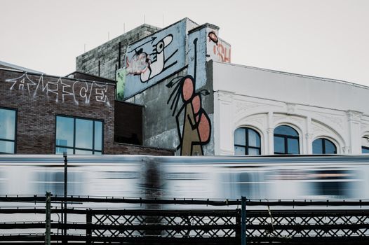 Dynamic scene of a speeding NYC subway passing colorful graffiti in an urban setting.