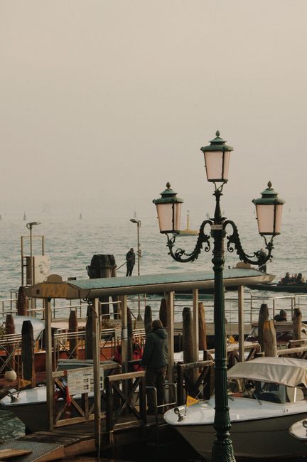 Calm Venice canal scene featuring an ornate street lamp and boats on a foggy day.