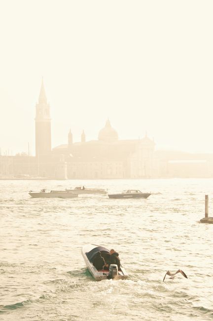 Sunlit view of Venice's canals with boats and iconic architecture in the background.