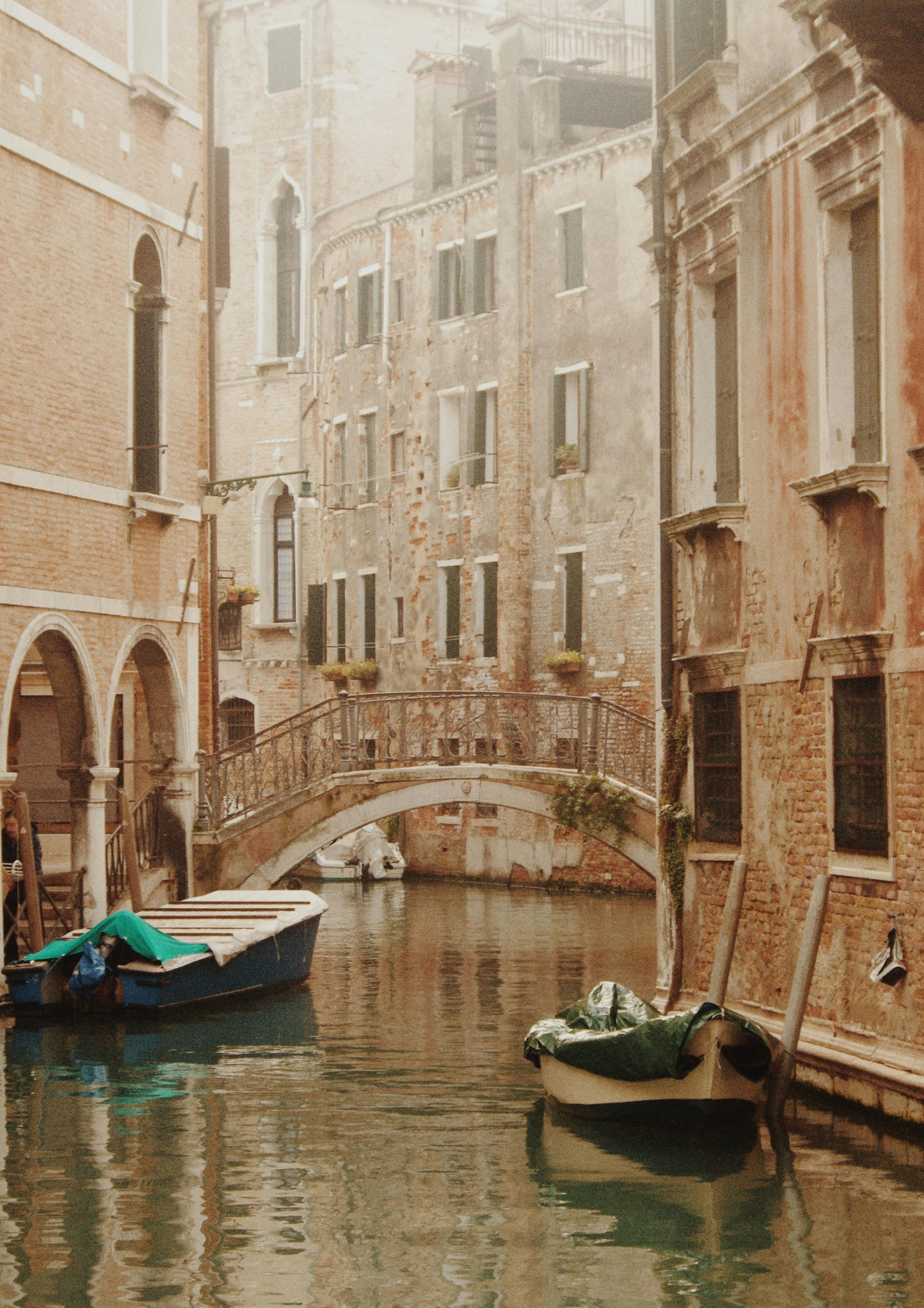 Charming view of a Venetian canal with historic buildings, a picturesque bridge, and moored boats.