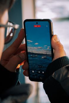 A person photographs a scenic view of boats on a seascape using a smartphone.