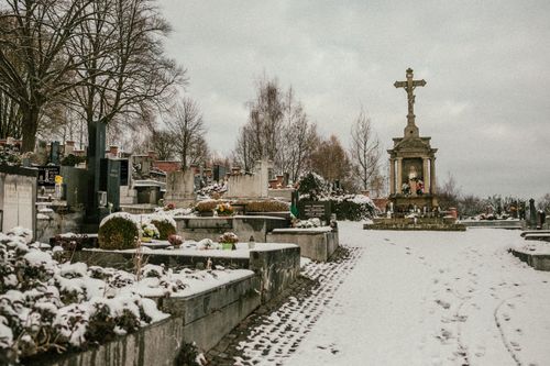 Free A tranquil cemetery blanketed in snow, featuring a prominent stone cross. Stock Photo