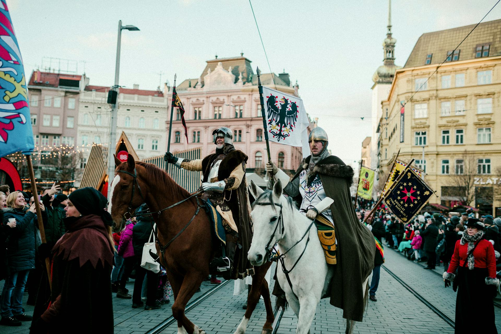 Medieval knights on horseback parade through a historic city square during a vibrant festival.