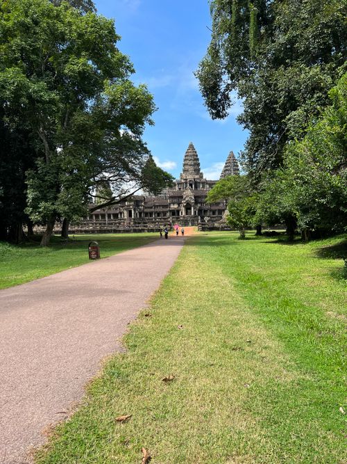 Free The majestic Angkor Wat Temple seen from a tree-lined path on a sunny day. Stock Photo