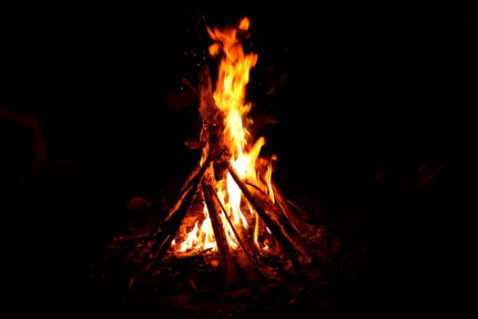 A vibrant campfire burning brightly at night, surrounded by logs and darkness.