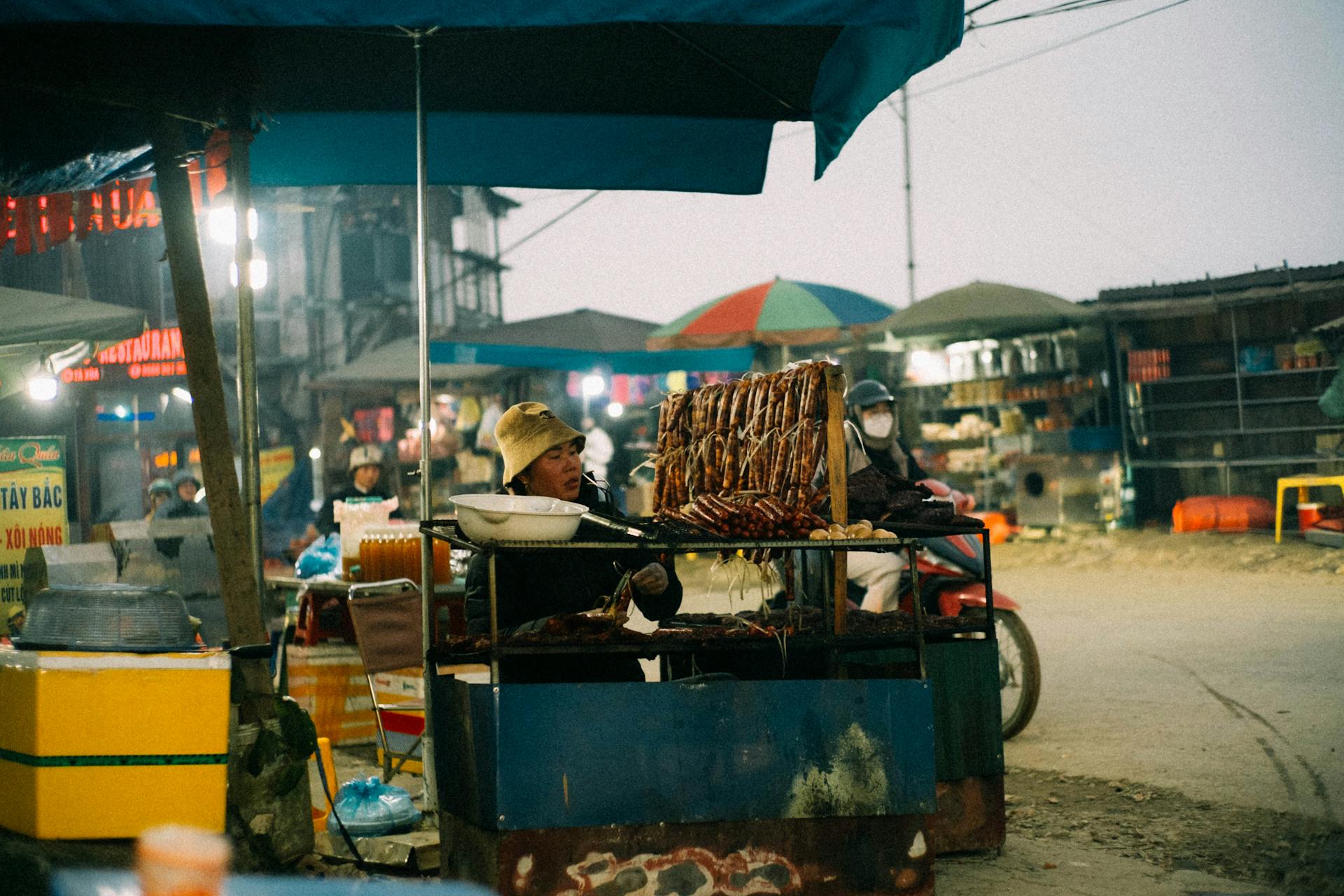 A bustling Asian street food market with diverse food stalls and a lively atmosphere captured at twilight.