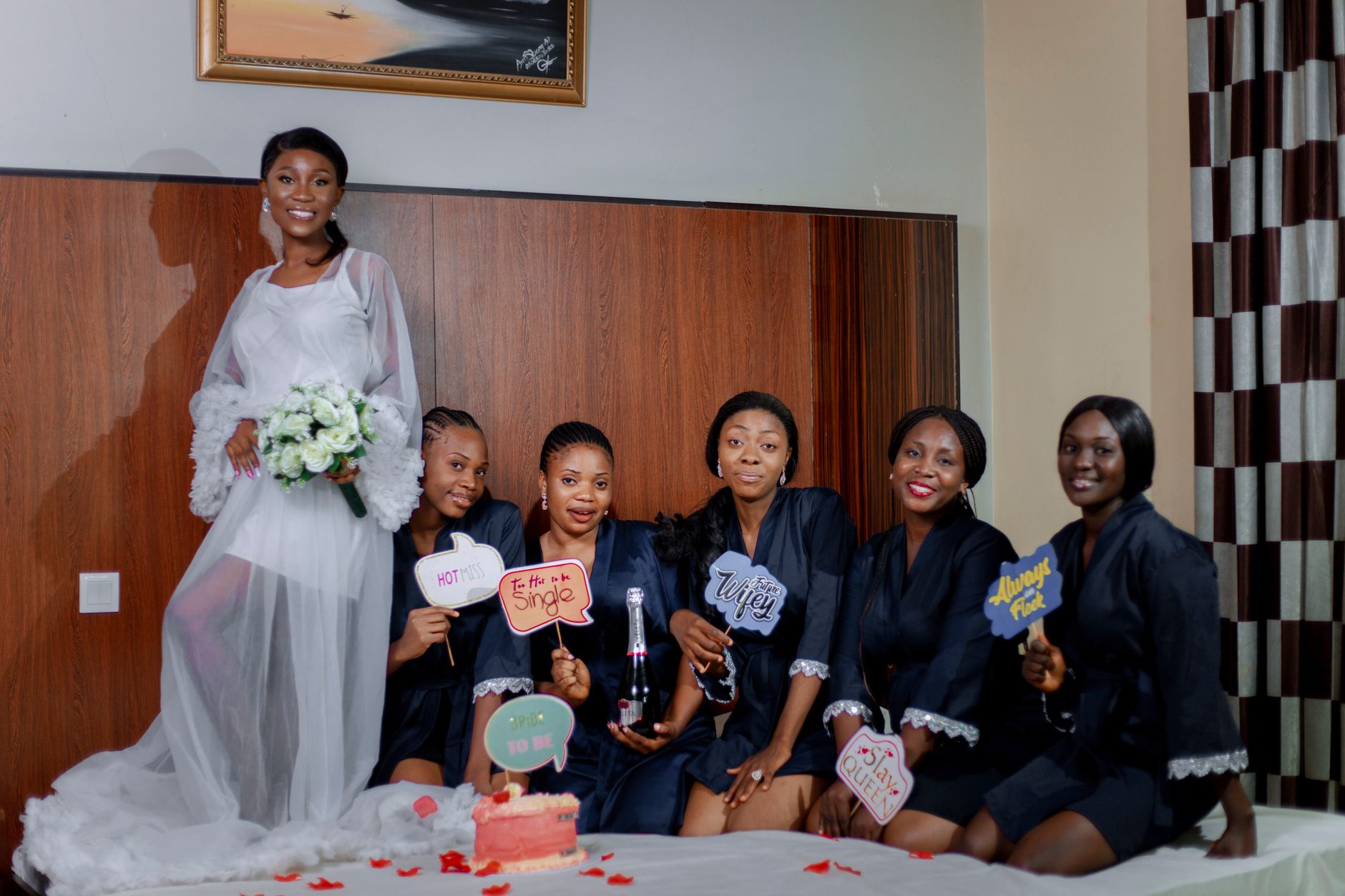 Joyful bridal party posing in a hotel room with signs and champagne.