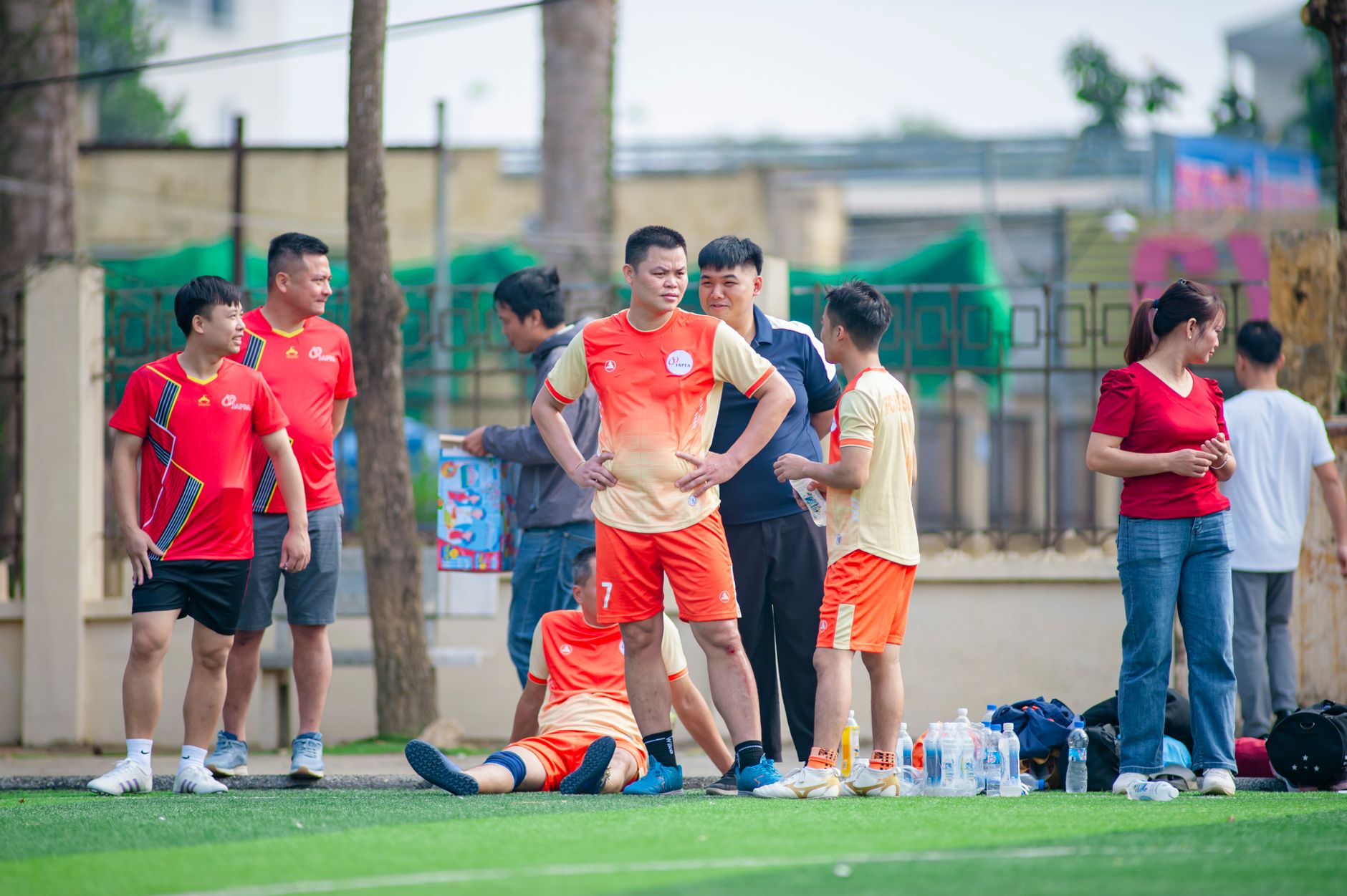 Amateur soccer team taking a break on the field in Hà Nội, engaging in lively discussion and camaraderie.
