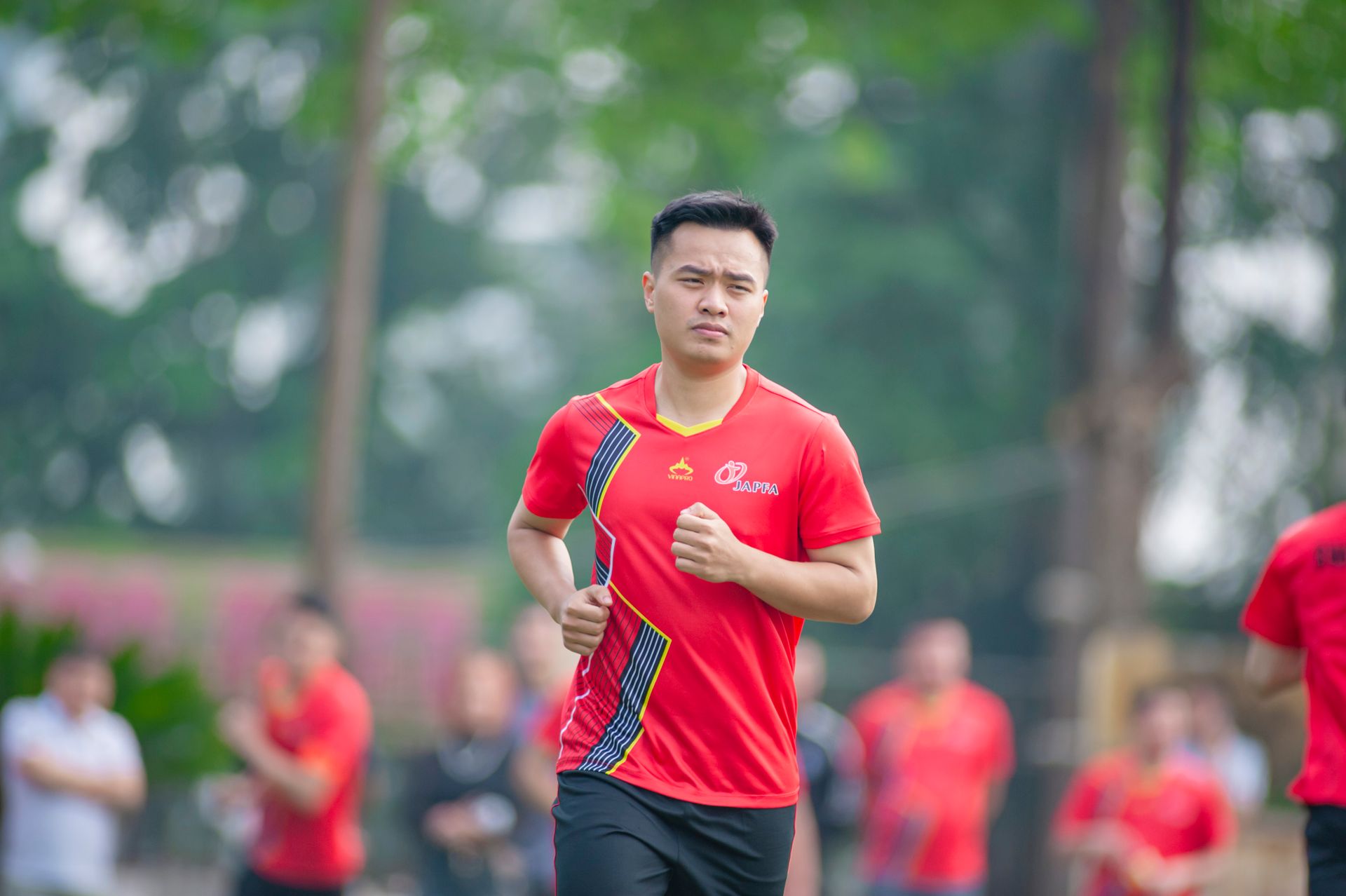 A young man jogging outdoors in a vibrant red shirt in a park in Hà Nội, Vietnam.