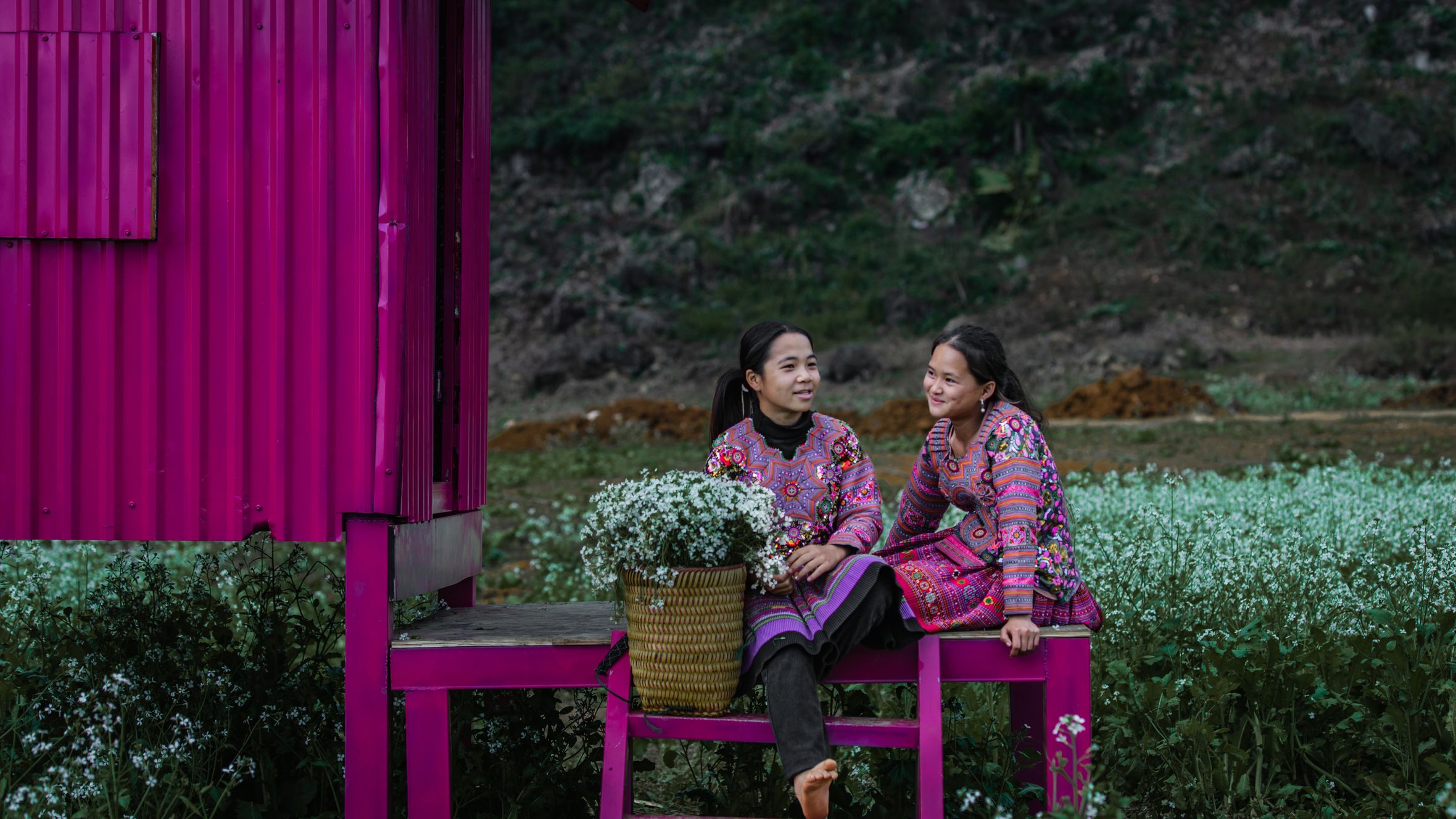 Two women in traditional attire enjoying time in a vibrant plum blossom field in Moc Chau.
