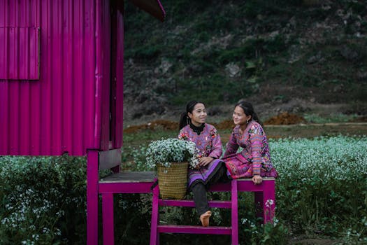 Two women in traditional attire enjoying time in a vibrant plum blossom field in Moc Chau.