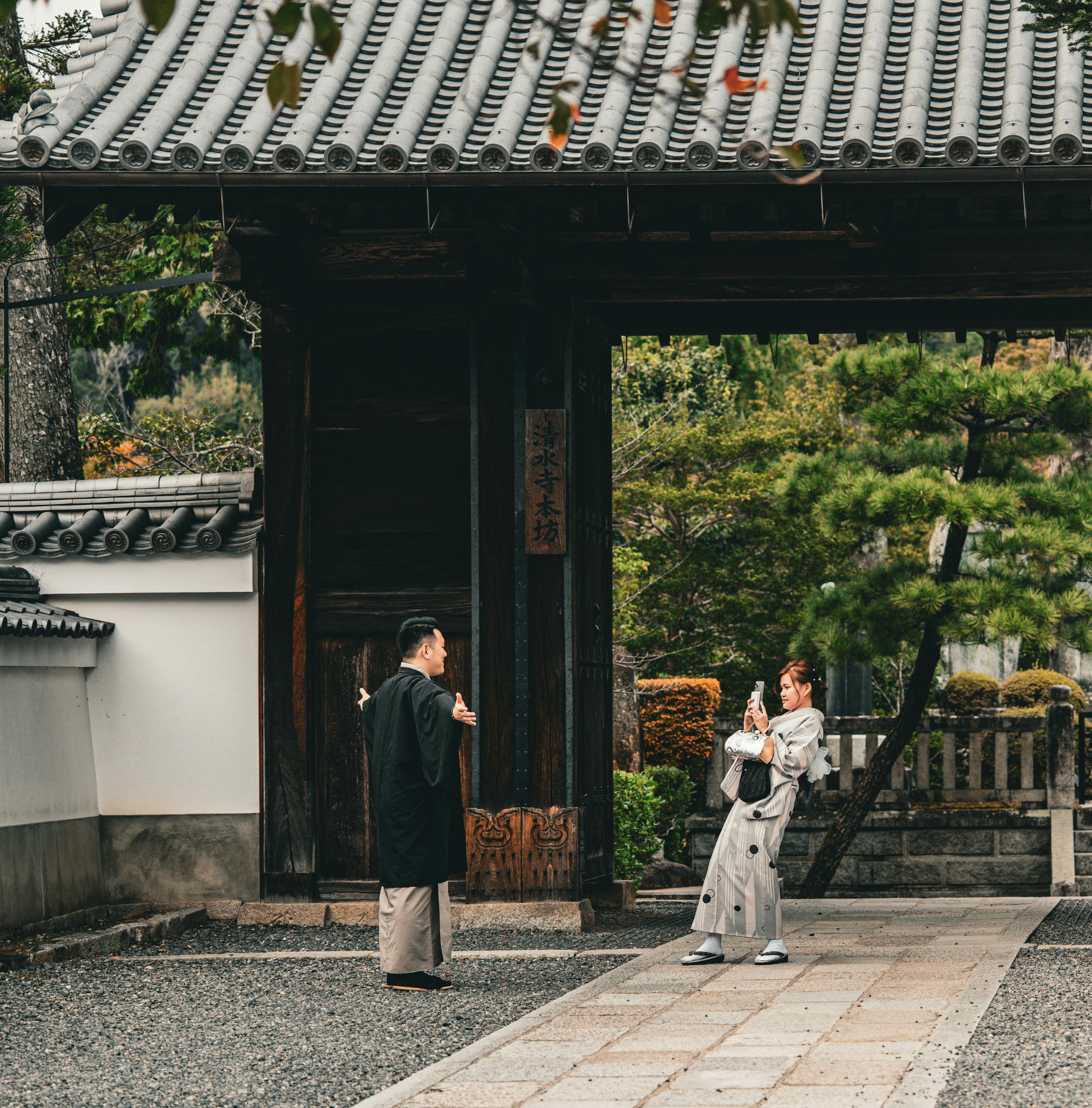 Two people in traditional Japanese attire near a historic gate in Kyoto, Japan.