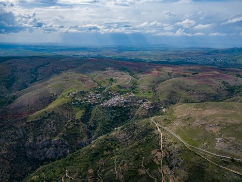 Free Breathtaking aerial view of a small village amidst rolling hills under a cloudy sky. Stock Photo