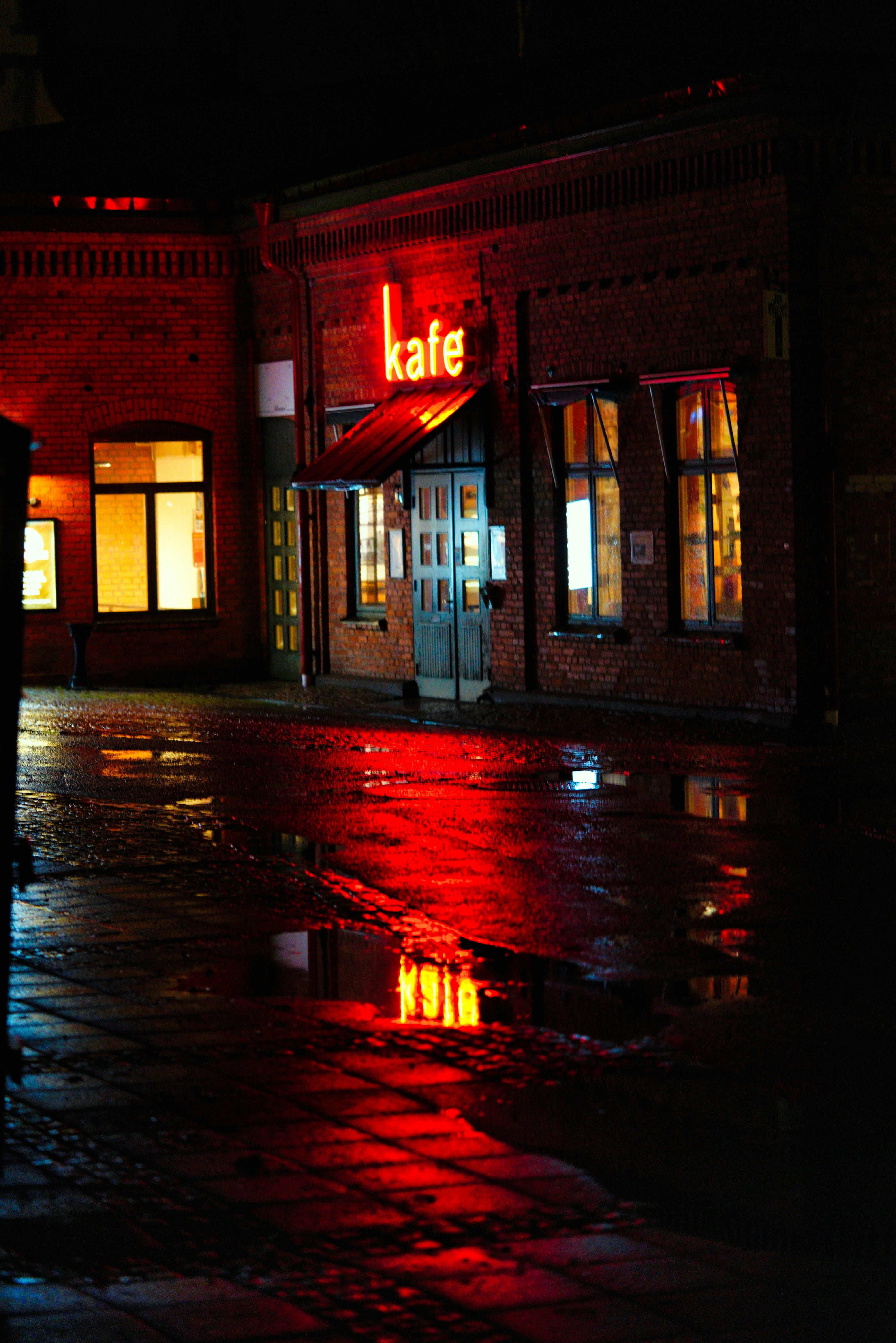 A vibrant neon café sign reflecting in the wet street at night in Jönköping, Sweden.