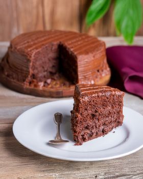 Close-up of a rich chocolate cake slice with a spoon on a wooden table.