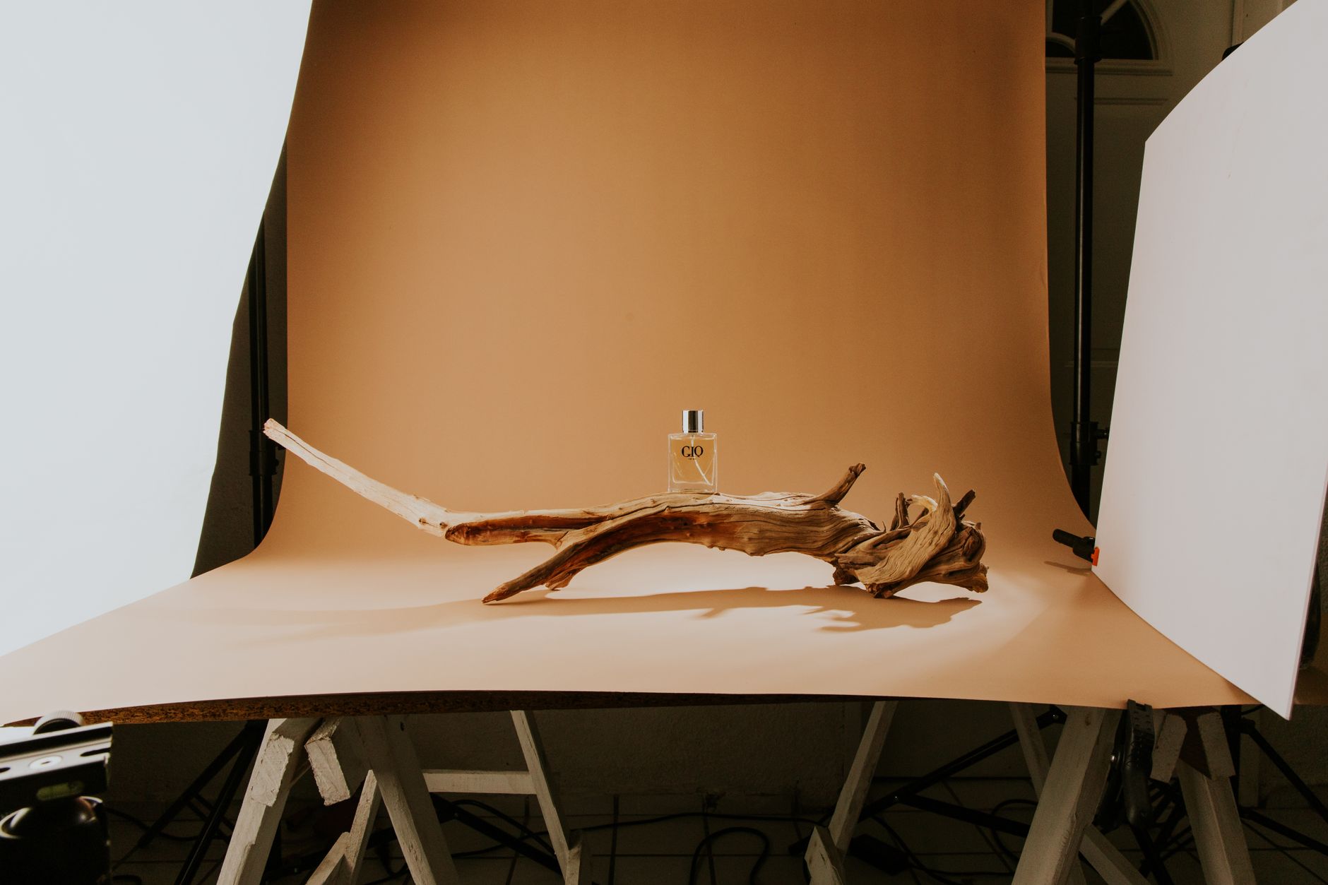 A stylish product photography setup featuring driftwood and a perfume bottle on a beige background.