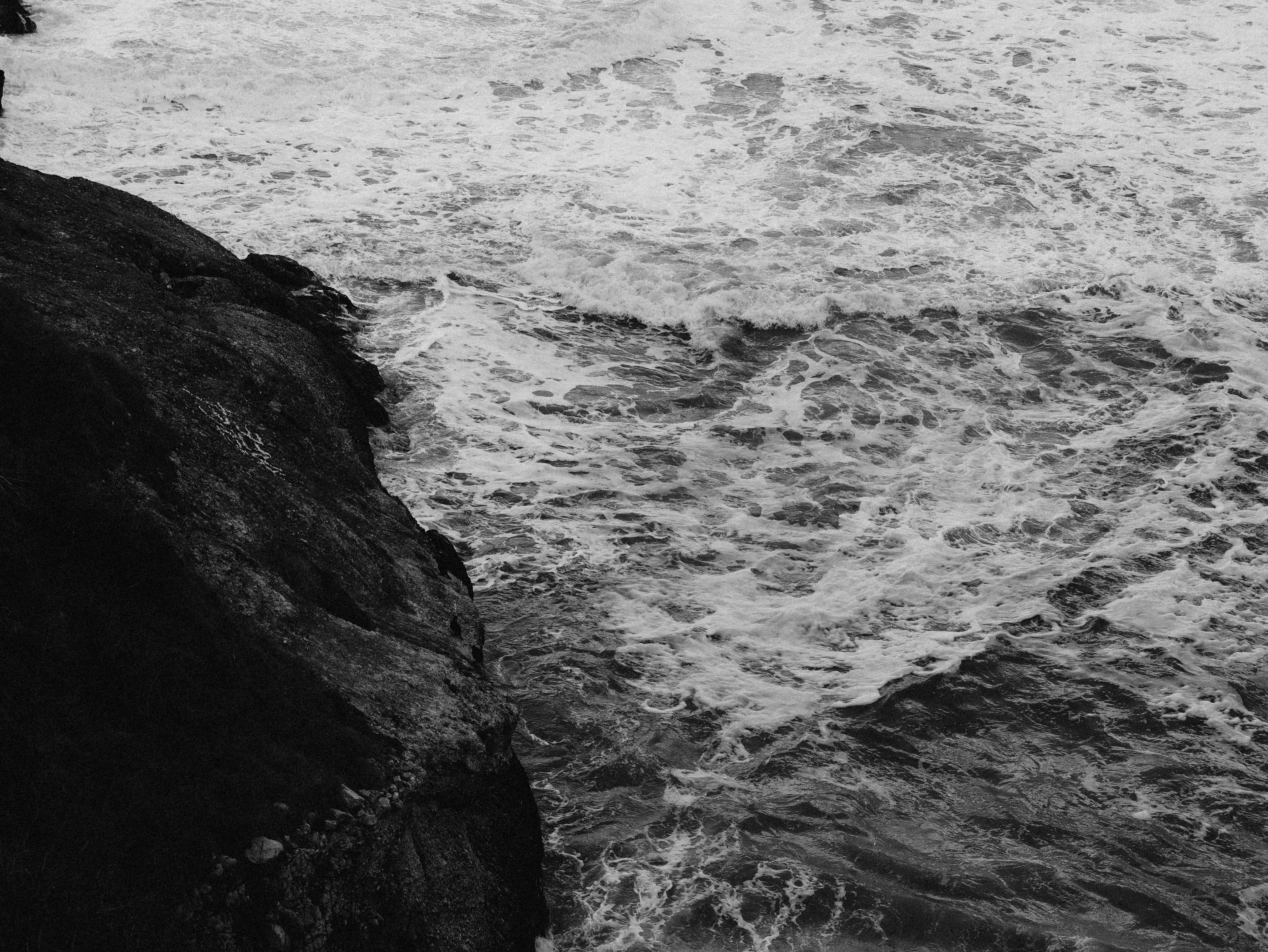 Black and white image capturing powerful ocean waves crashing against rugged cliffs.