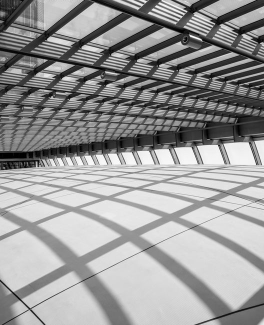 Modern glass and steel architecture with geometric patterns and shadows creates a futuristic interior space.