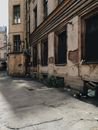 一条阳光明媚的小巷，紧邻一座废弃建筑，展现出城市的衰败与年久失修
