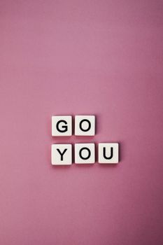 Inspirational 'Go You' message with letter tiles on a pink background.