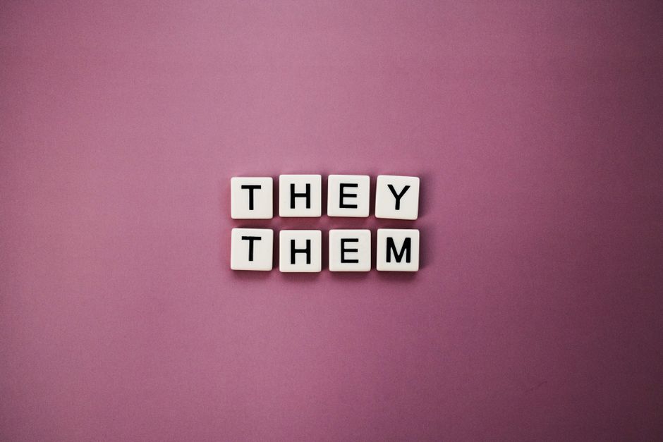 Non-binary pronouns 'they them' displayed with letter tiles on a pink backdrop.