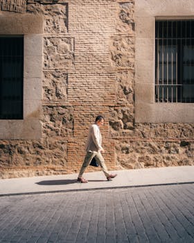 A man in a white suit walks beside a historic stone wall in Toledo, Spain.