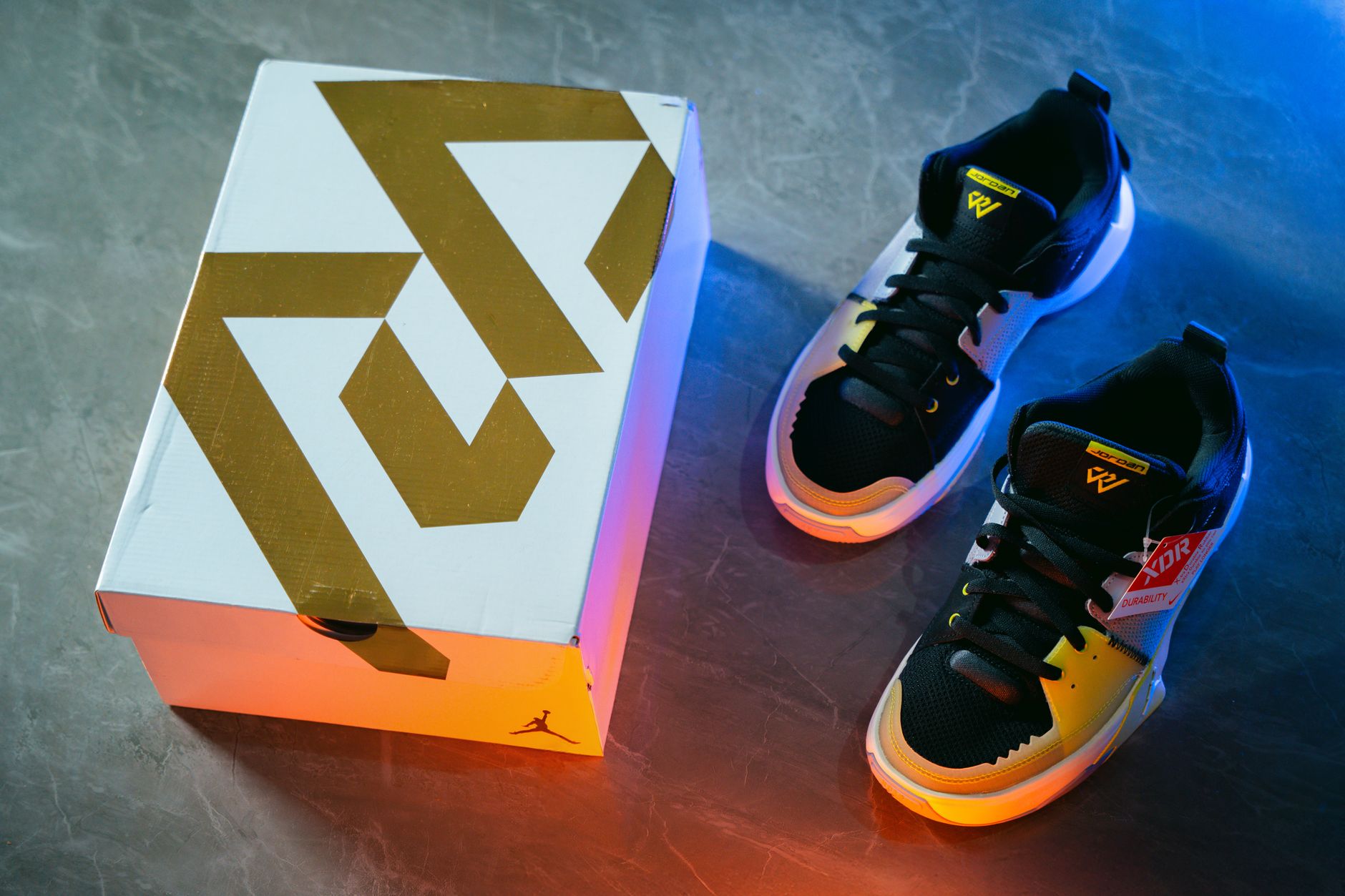 Black and yellow sneakers displayed with a geometric design box on a marble background.