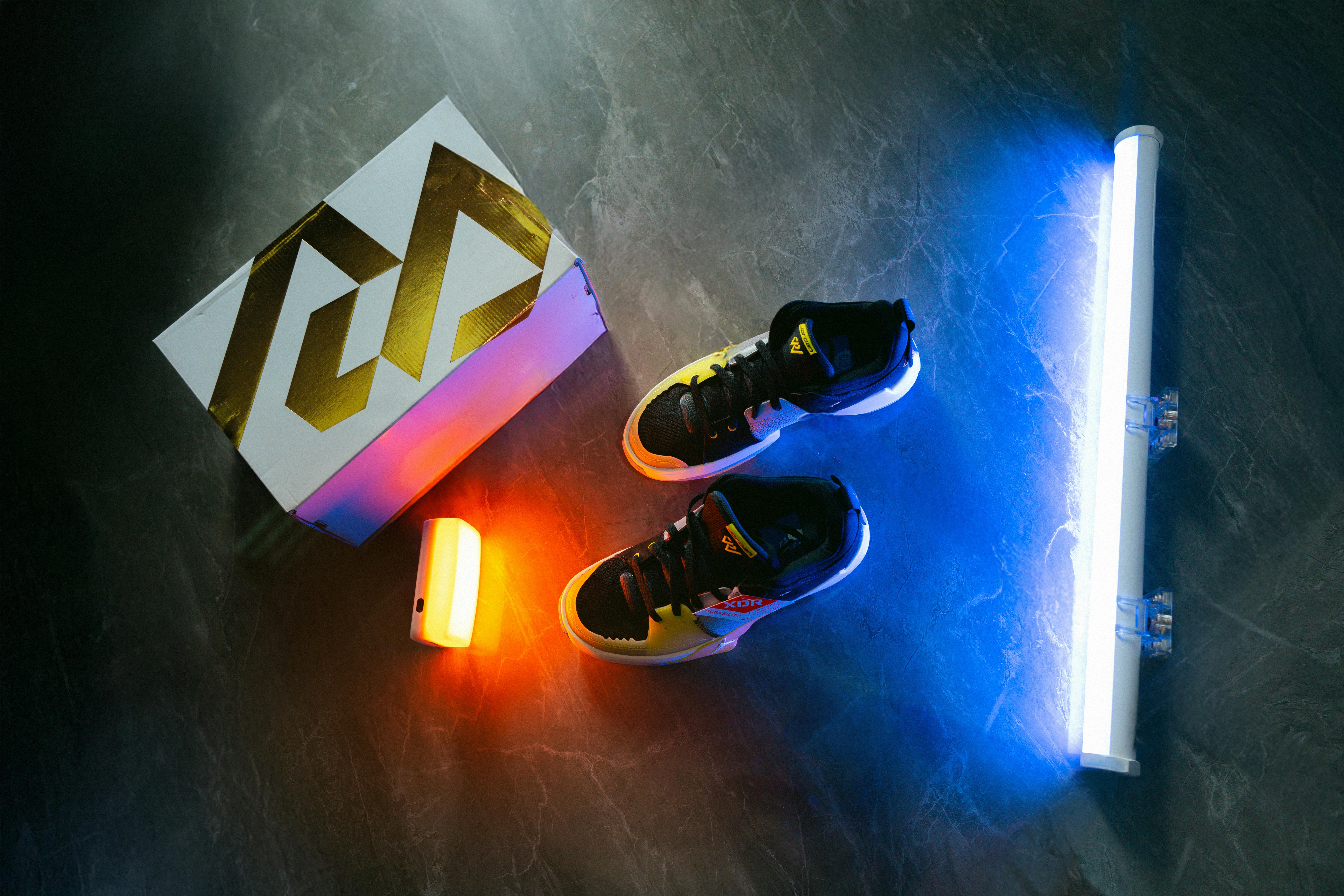 Zadarmo Tenisky osvetlené žiarivým neónovým osvetlením na tmavom mramorovom povrchu pre dynamickú estetiku. Fotka z fotobanky