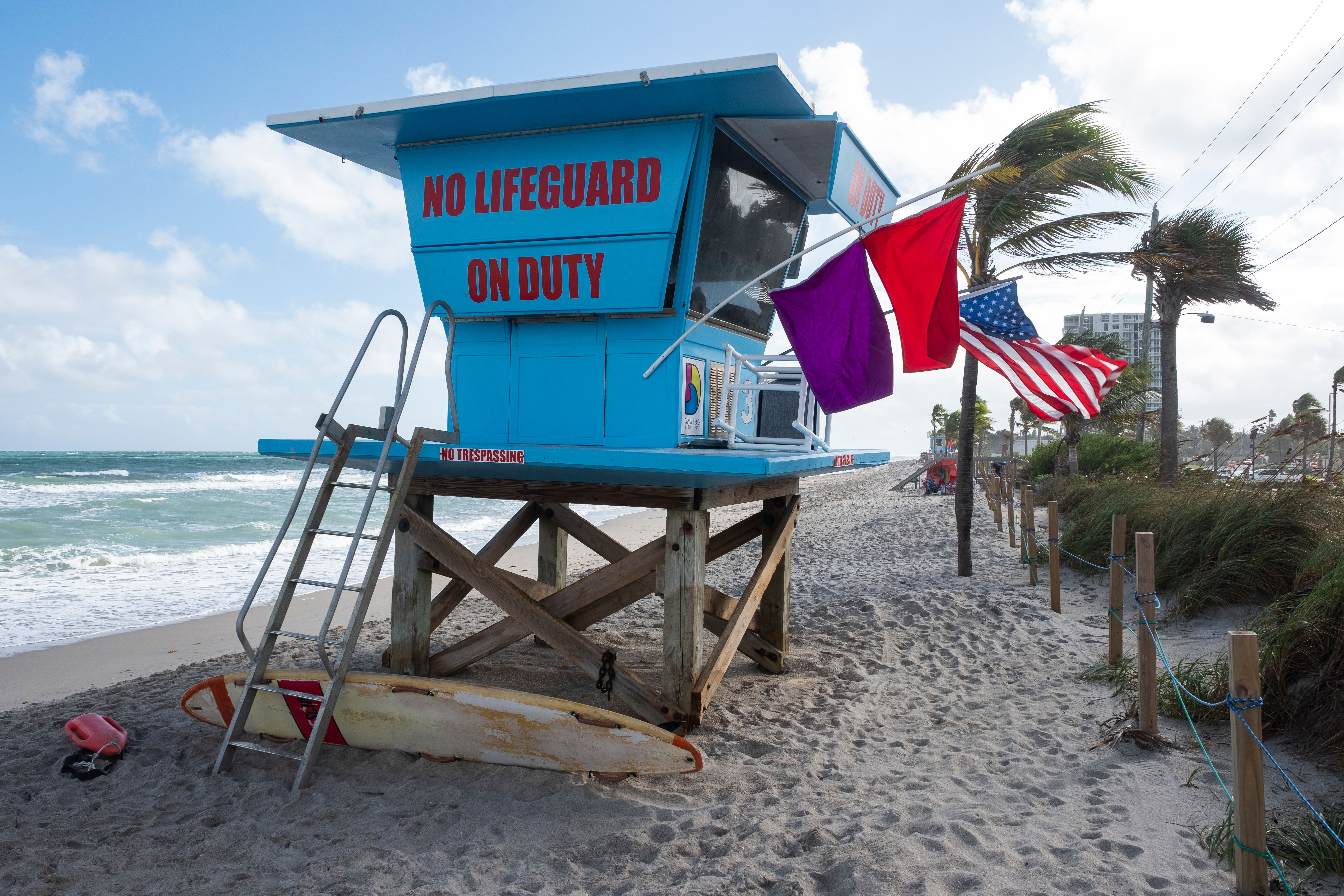 A vibrant lifeguard tower stands on a sandy beach in Florida, USA, with flags waving in the wind.